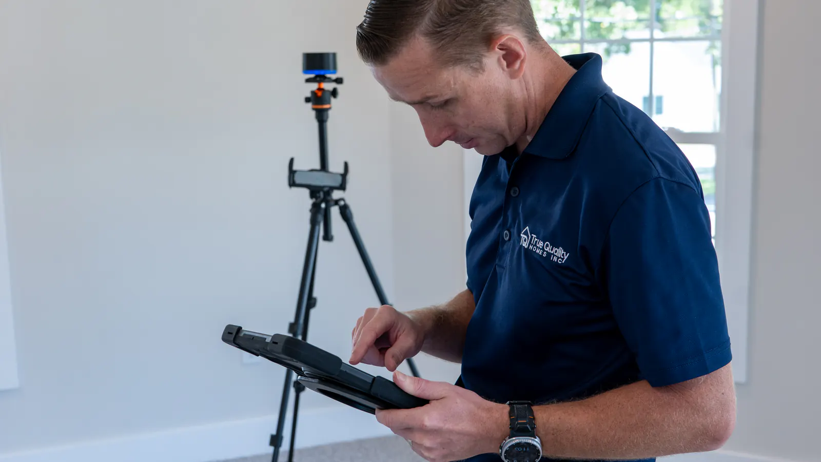 A True Quality Homes team member running an iMapper scan on his own, tablet in hand, with the Racer 3+ on its tripod behind him